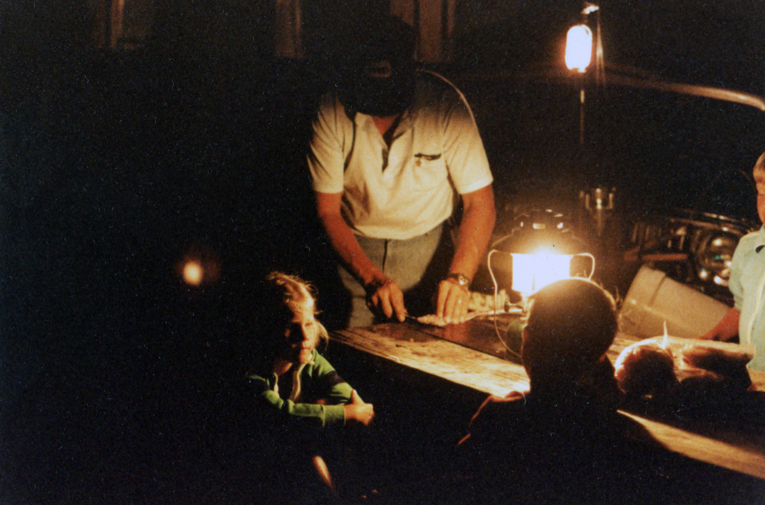 A young Annie Woodford, in a photograph taken by her mother, sits as her father cleans fish by lanternlight.