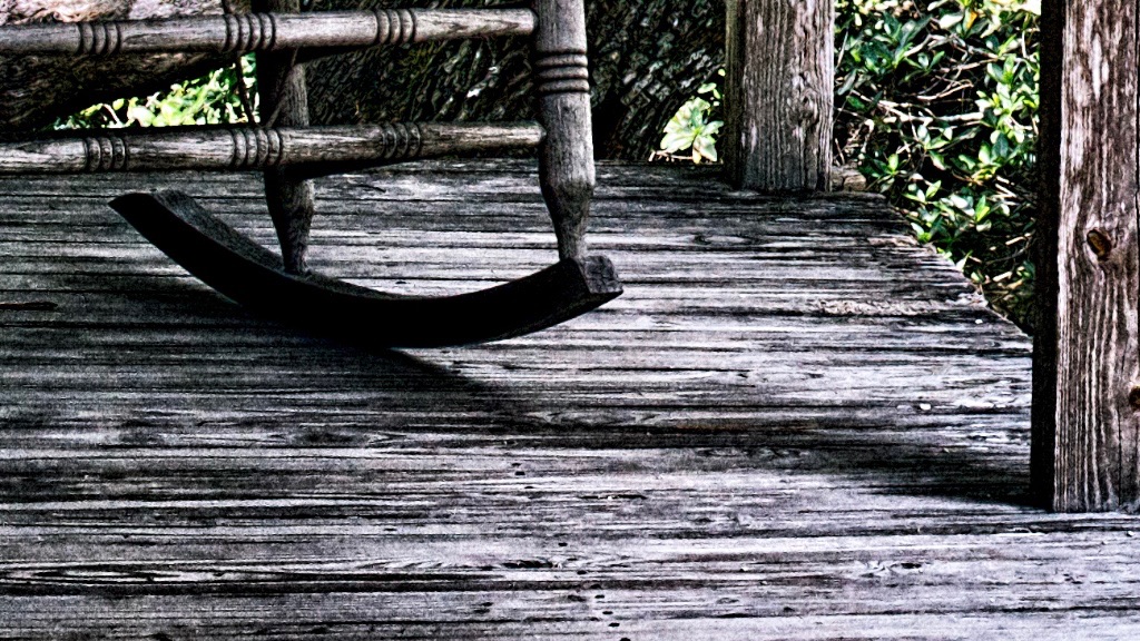 Looking across old wooden porch towards an empty rocking chair with wicker back in tropical estero, florida setting.