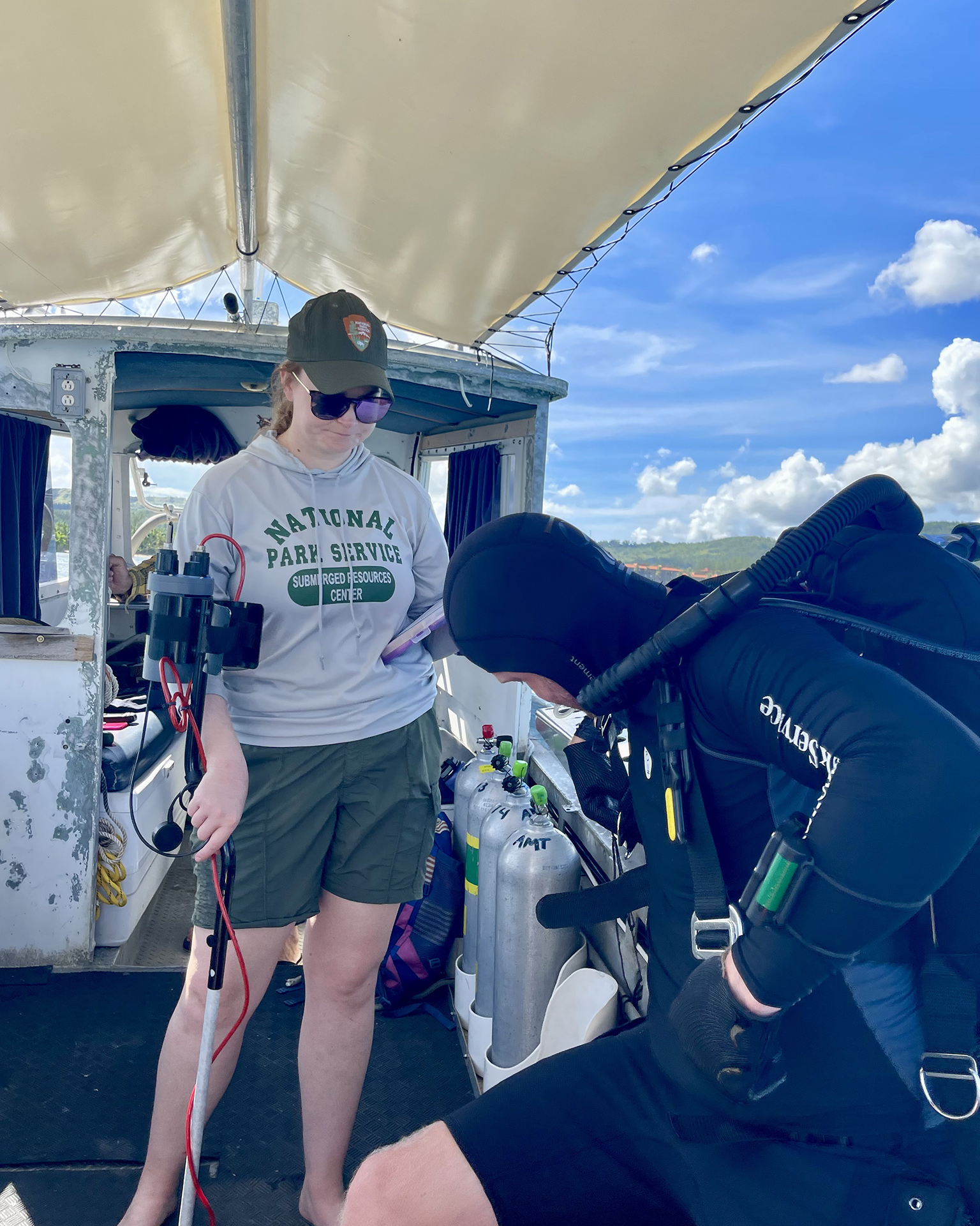 CONDENSED-NPRSRC-ON-BOAT On a dive boat off Guam, National Park Service Submerged Resources Center team leader and underwater archaeologist Annie Nunn helps fellow archaeologist Matt Hanks prepare to dive (photograph by Russell Worth Parker).